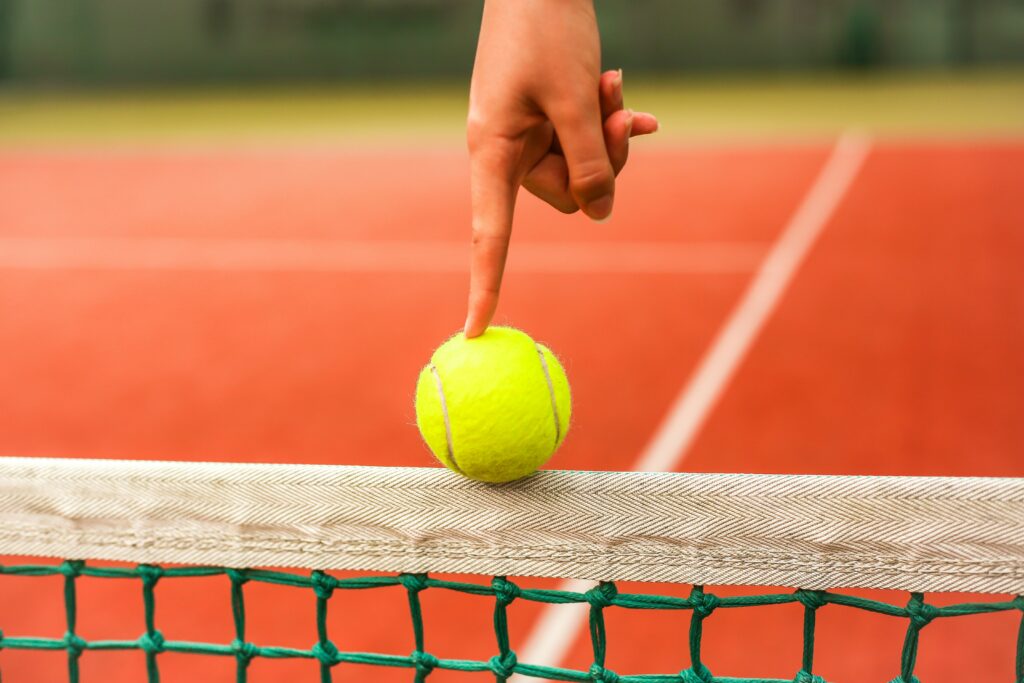 balle de tennis sur un filet tenue par un doigt